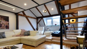 A modern living room with a sectional sofa, a coffee table, and a staircase with wooden beams. - Libertas Apartment Zagreb (Zagreb)