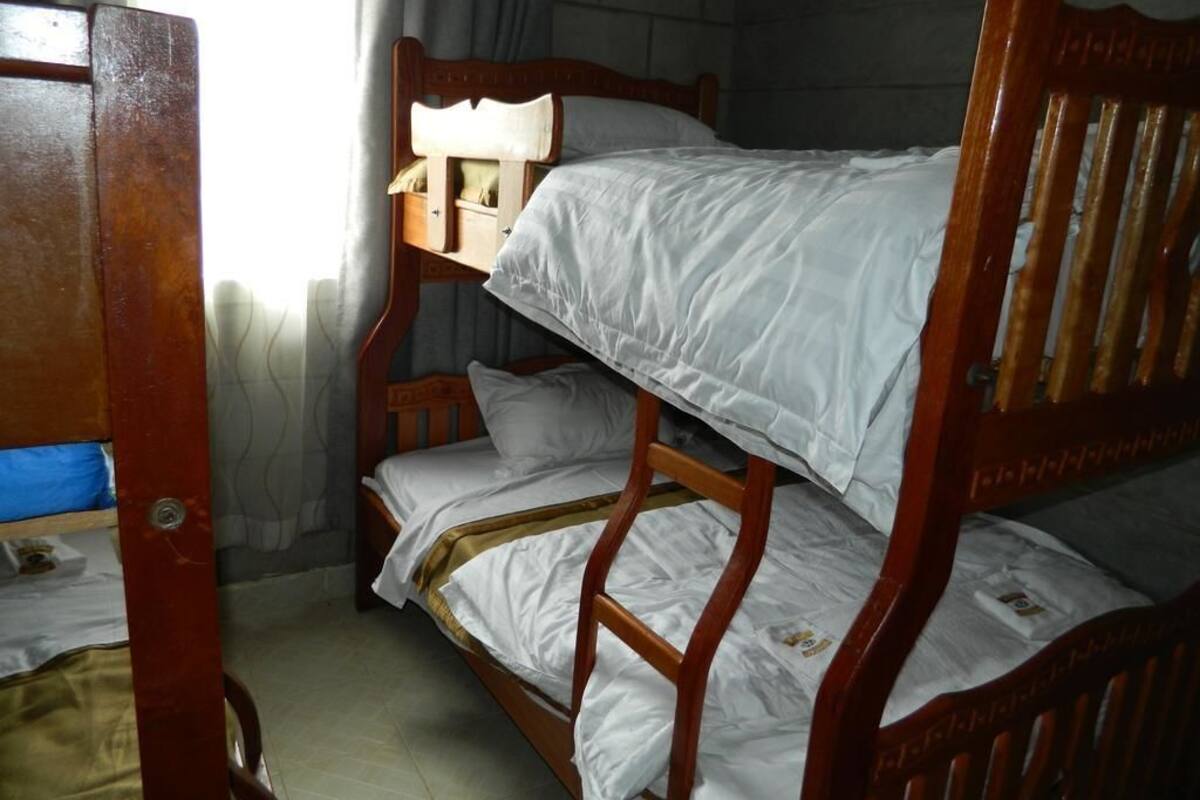 A bunk bed with a wooden headboard, a small wooden chair, and a window with curtains.