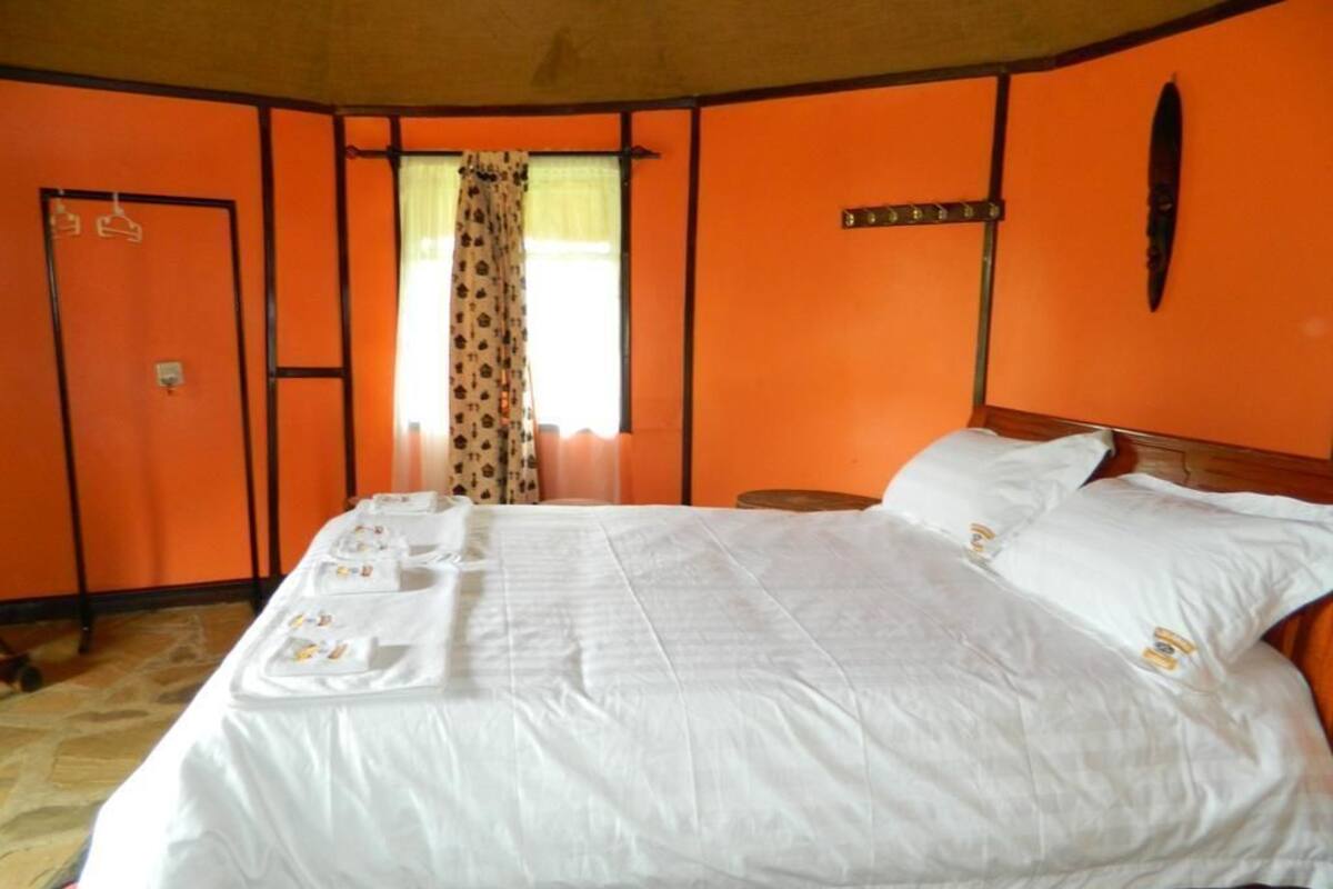 A room with an orange wall, a bed with white bedding, a wooden headboard, and a window with curtains.