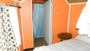 Un dormitorio con pared naranja, cama con ropa blanca, taburete de madera y cortina estampada.
