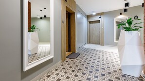 Passadís modern amb paviment estampat, un mirall gran, una planta en test i una porta amb el símbol de número.