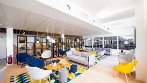 A modern, spacious lounge area with a variety of seating options, including sofas and chairs, and a large window providing a view of the outdoors. - Staycity Aparthotels, Near Disneyland® Paris (Bailly-Romainvilliers)