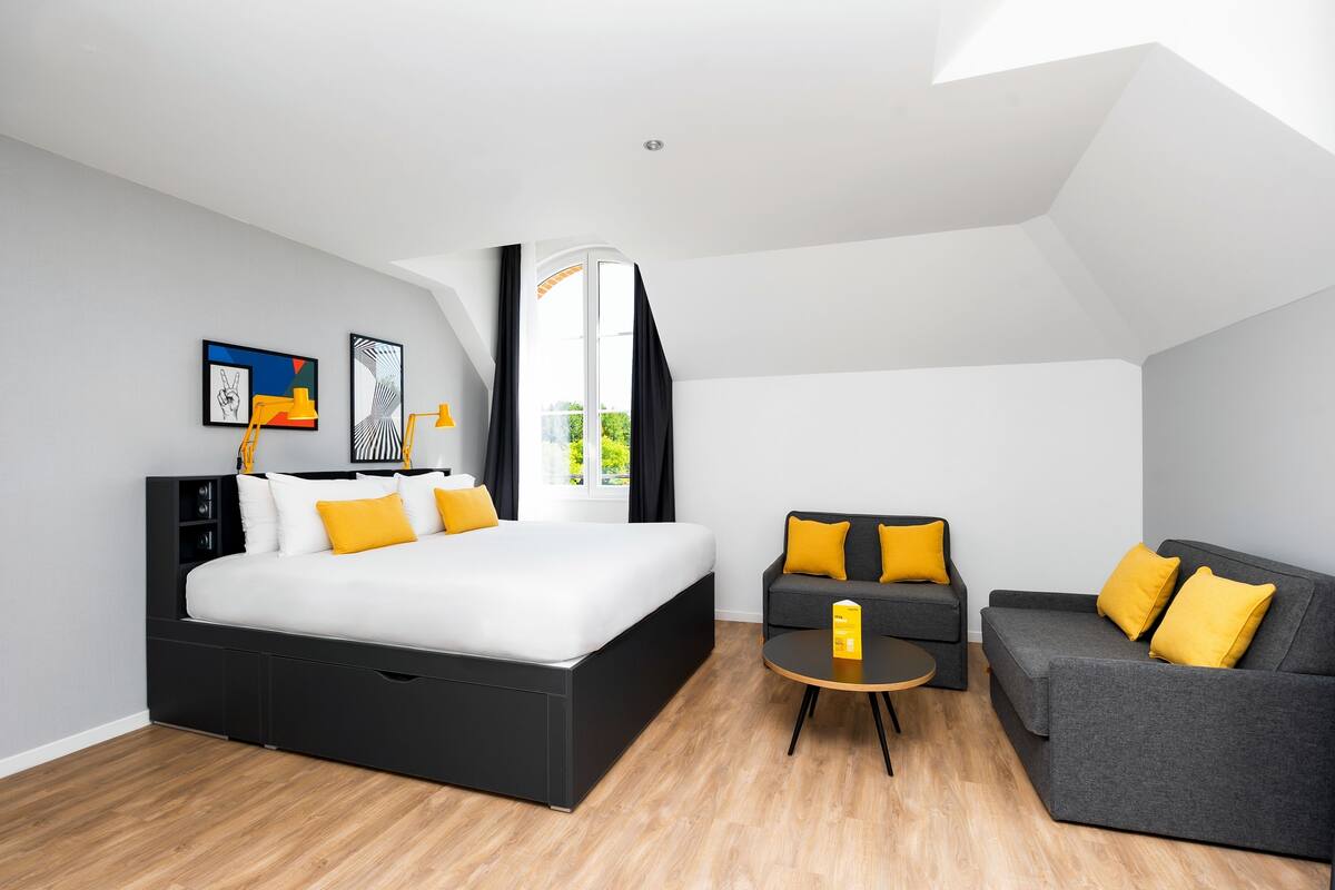A modern bedroom with a large bed, two sofas, a small table, and artwork on the walls.