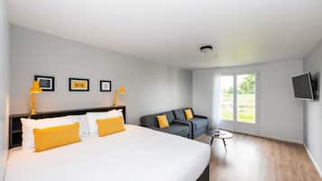 Une chambre d’hôtel avec un grand lit, un canapé, une petite table et un téléviseur fixé au mur.