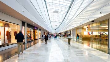 A spacious indoor shopping mall with a high ceiling and a glass ceiling allowing natural light.