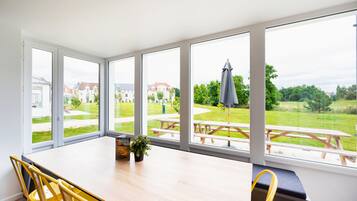 Una habitación luminosa con ventanas amplias, una mesa de madera, sillas amarillas y un banco.