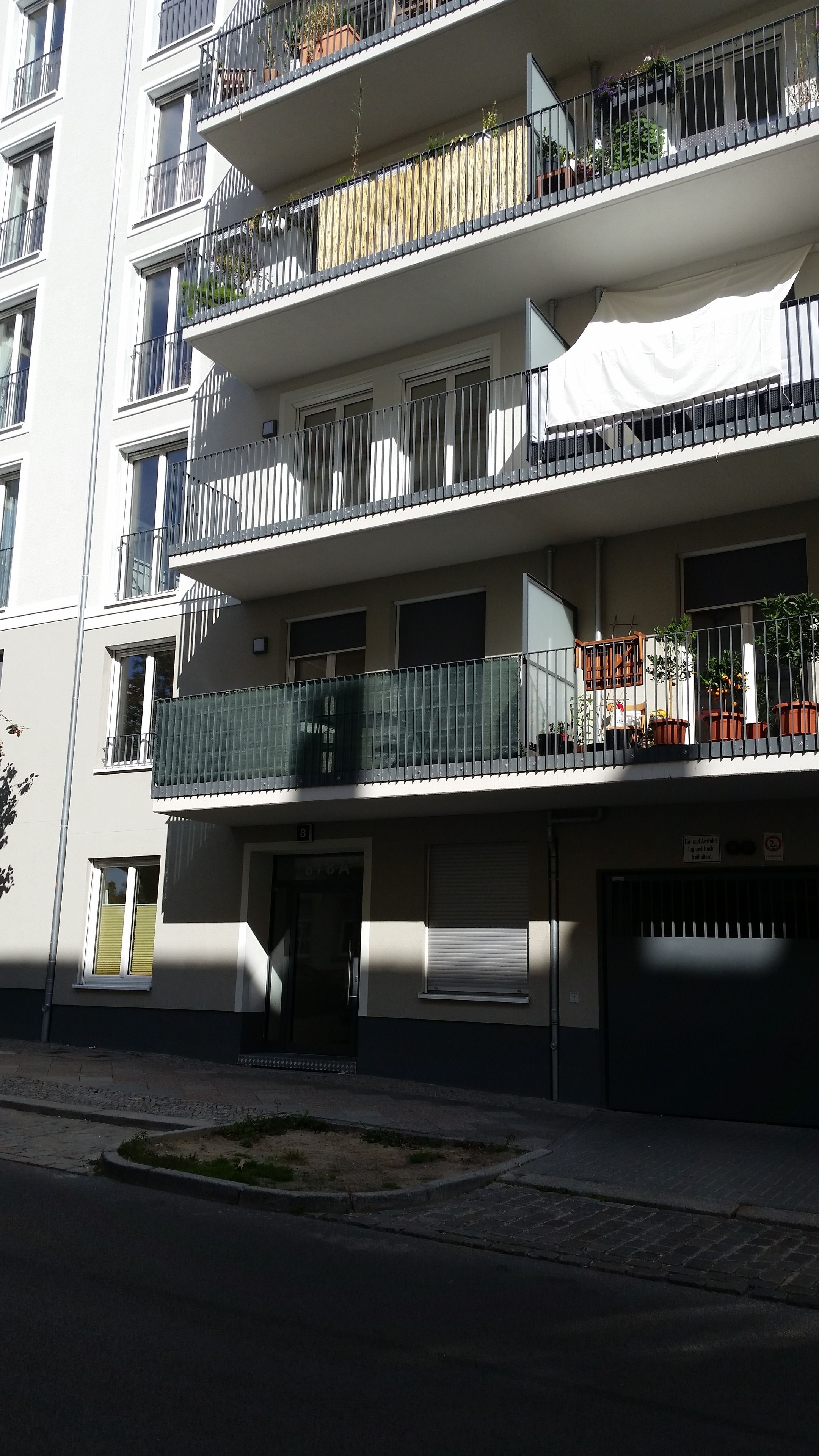 Ein mehrgeschossiges Wohngebäude mit Balkonen, Pflanzkübeln und einer Garage.
