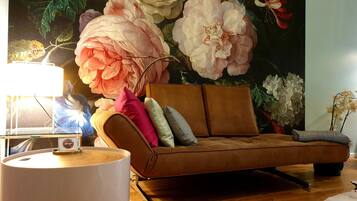Ein modernes Wohnzimmer mit einem braunen Sofa, einem runden weißen Tisch und einer großen Wandmalerei mit floralem Muster.