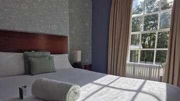 A neatly made bed with a rolled towel, a green pillow, and a white pillow. There is a nightstand with a lamp beside the bed.