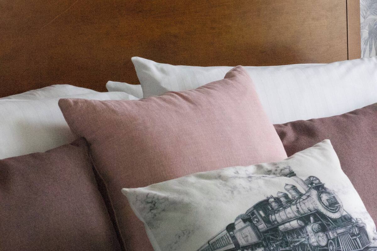 Ein Bett mit vielen Kissen, einem Holz-Kopfteil und blumigem Wandpapier.