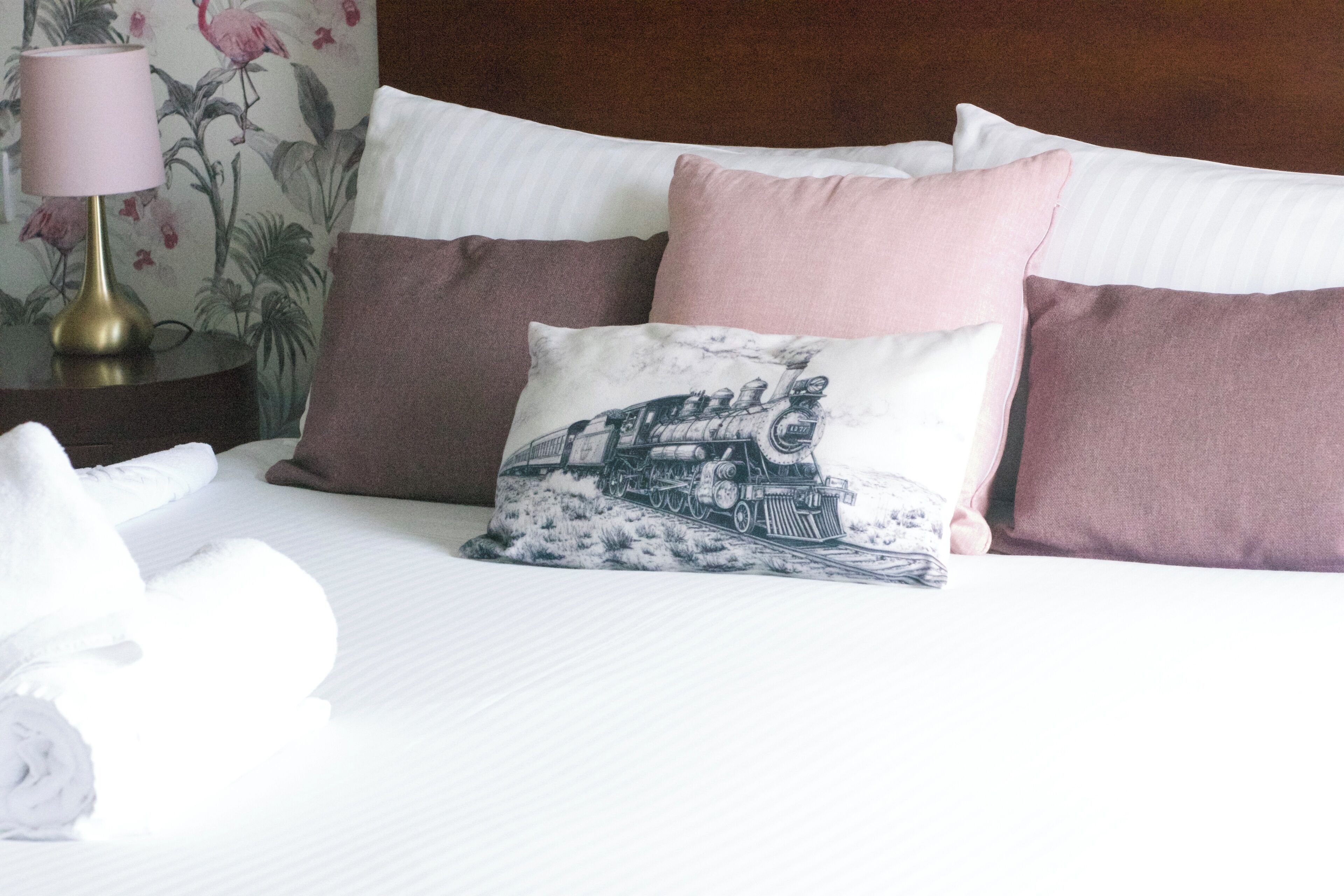 A neatly made bed with pillows, a lamp, and a floral wallpaper.