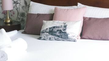 A neatly made bed with pillows, a lamp, and a floral wallpaper.