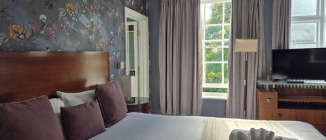 Una habitación de hotel con una cama grande, televisión y ventana con cortinas.