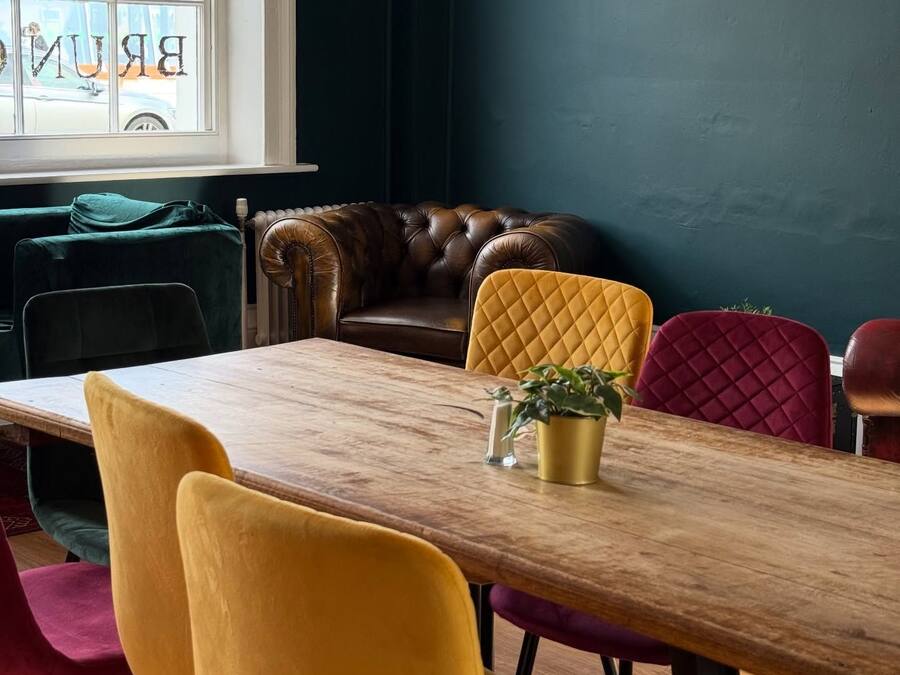 Een eetgedeelte met een houten tafel, kleurrijke stoelen, een leren bank en uitzicht door een raam.