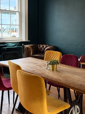 A dining area with a wooden table, colorful chairs, a leather sofa, and a view through a window. - The Great Western Hotel (Taunton)
