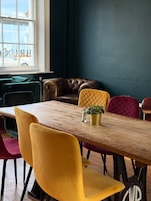 A dining area with a wooden table, colorful chairs, a leather sofa, and a view through a window.