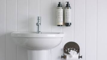 Un lavabo blanco con grifo, dos botellas de artículos de tocador y un dispensador de papel higiénico con un diseño decorativo.