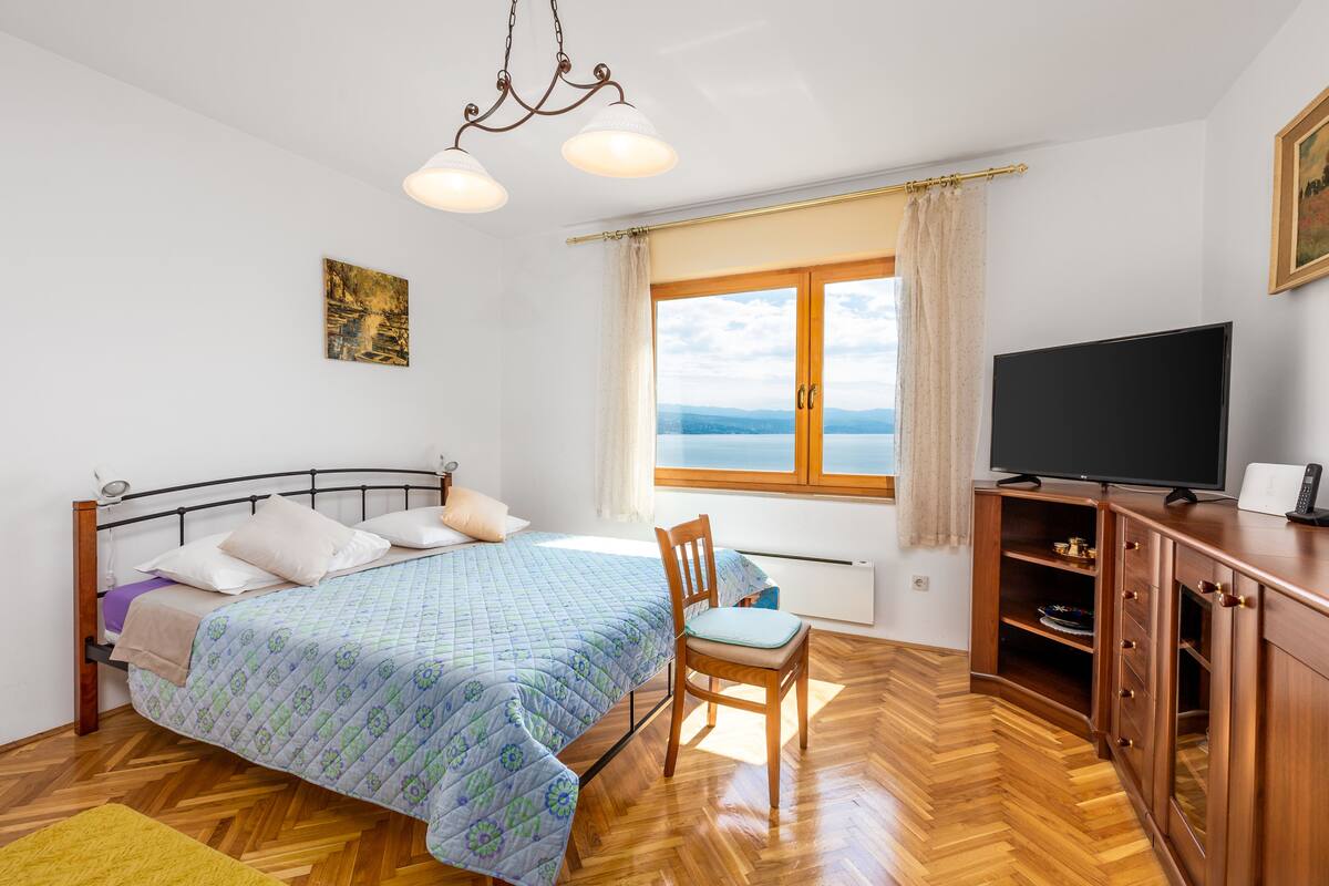Une chambre à coucher avec un lit, une chaise, une télévision et une fenêtre donnant sur un paysage agréable.