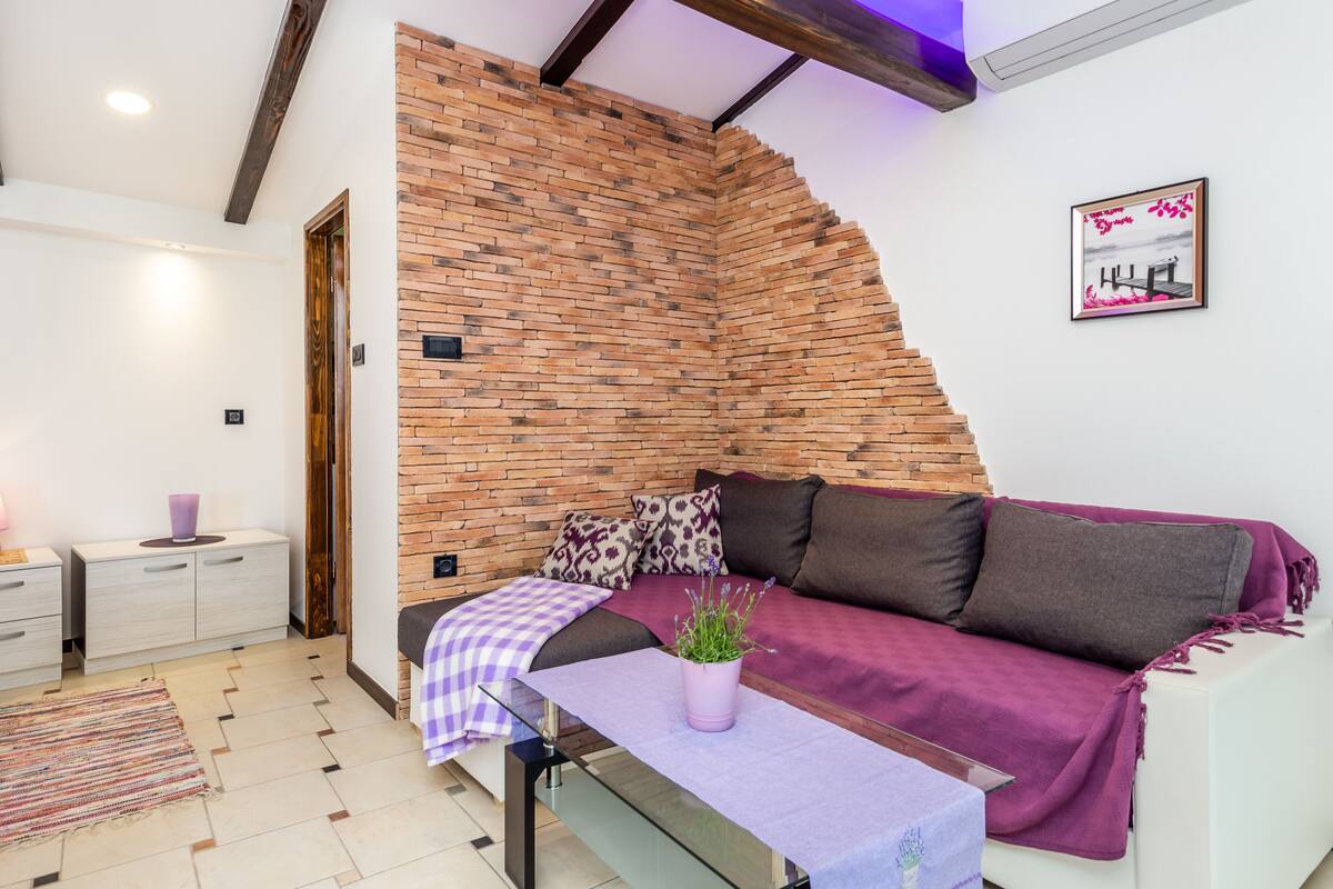 Un salon moderne avec un mur d’accent en briques, un canapé blanc et une petite table sur laquelle est posée une plante.