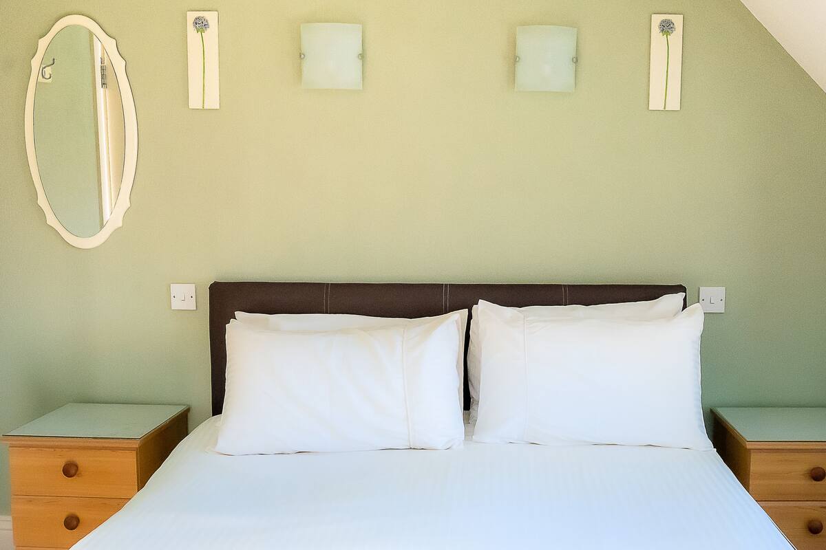 A bedroom with a bed, two nightstands, a mirror, and three wall-mounted lights.
