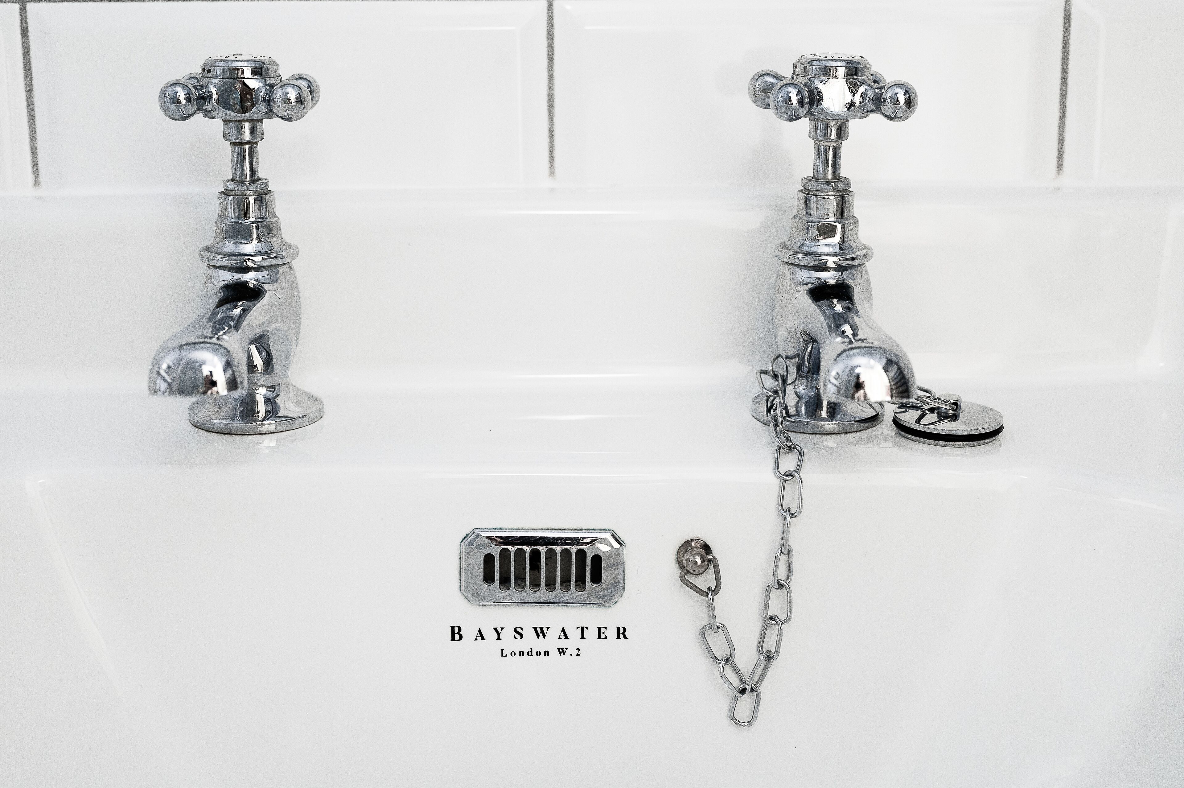 A bathroom with two chrome faucets and a drain cover labeled "BAYSWATER London W.2".