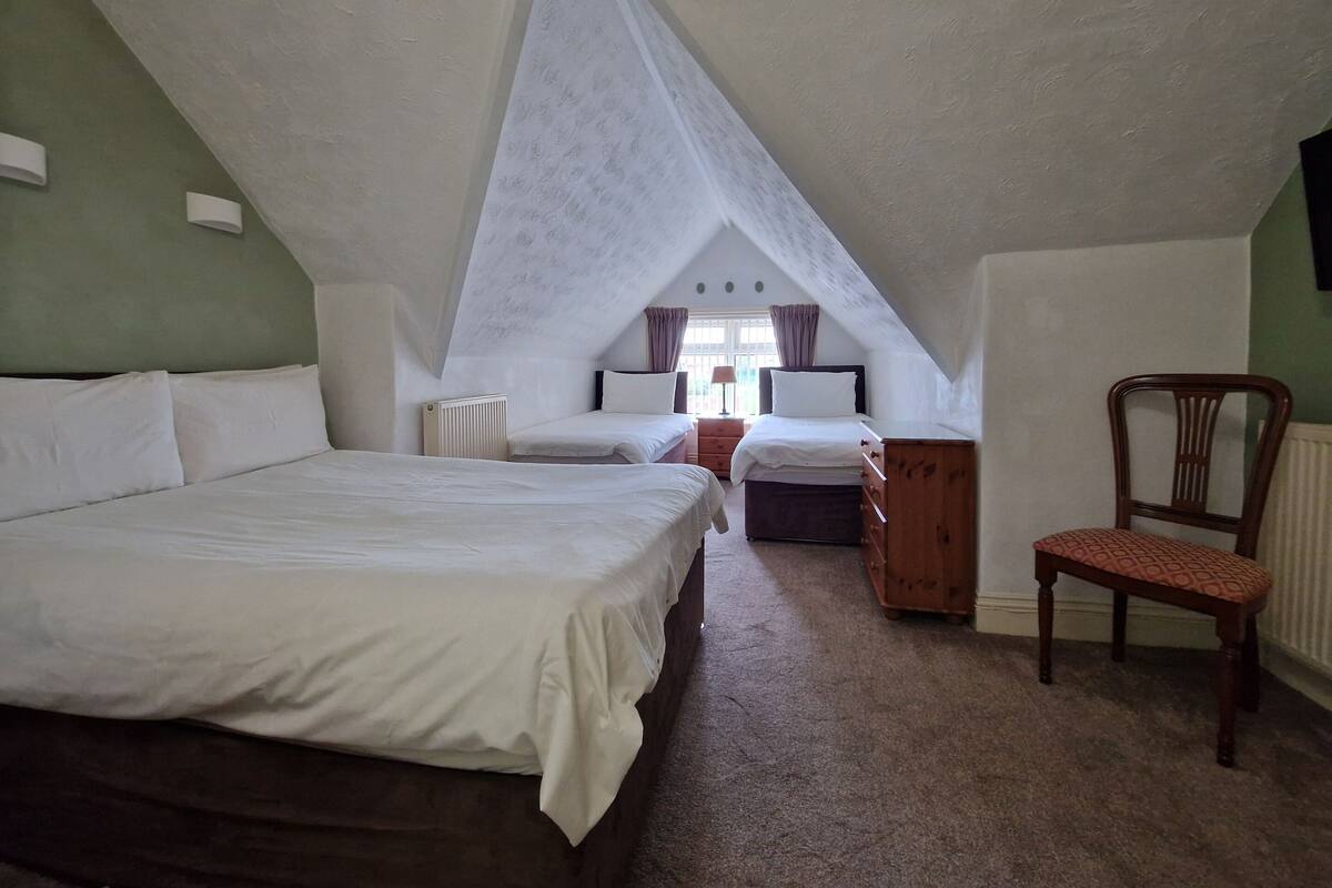 A bedroom with a sloped ceiling, a large bed, a smaller bed, a chair, and a dresser.