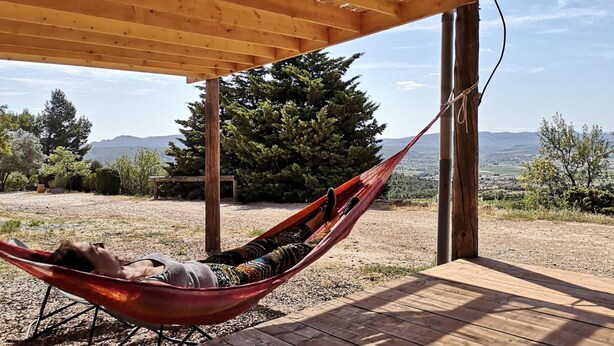 Una hamaca bajo una pérgola de madera con vistas a un paisaje montañoso.