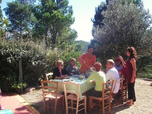 A group of people dining outdoors at a round table with a green tablecloth, surrounded by natural scenery and trees. - Yourte Nature Saint Roch (Tuchan)