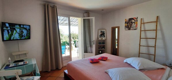 A bedroom with a bed, a desk with a chair, a television, a window with curtains, and a door leading to an outdoor area. - Villa des Delices (Grimaud)