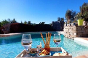 A poolside dining setup with a tray of food, glasses, and a view of the pool and landscape. - Villa des Delices (Grimaud)