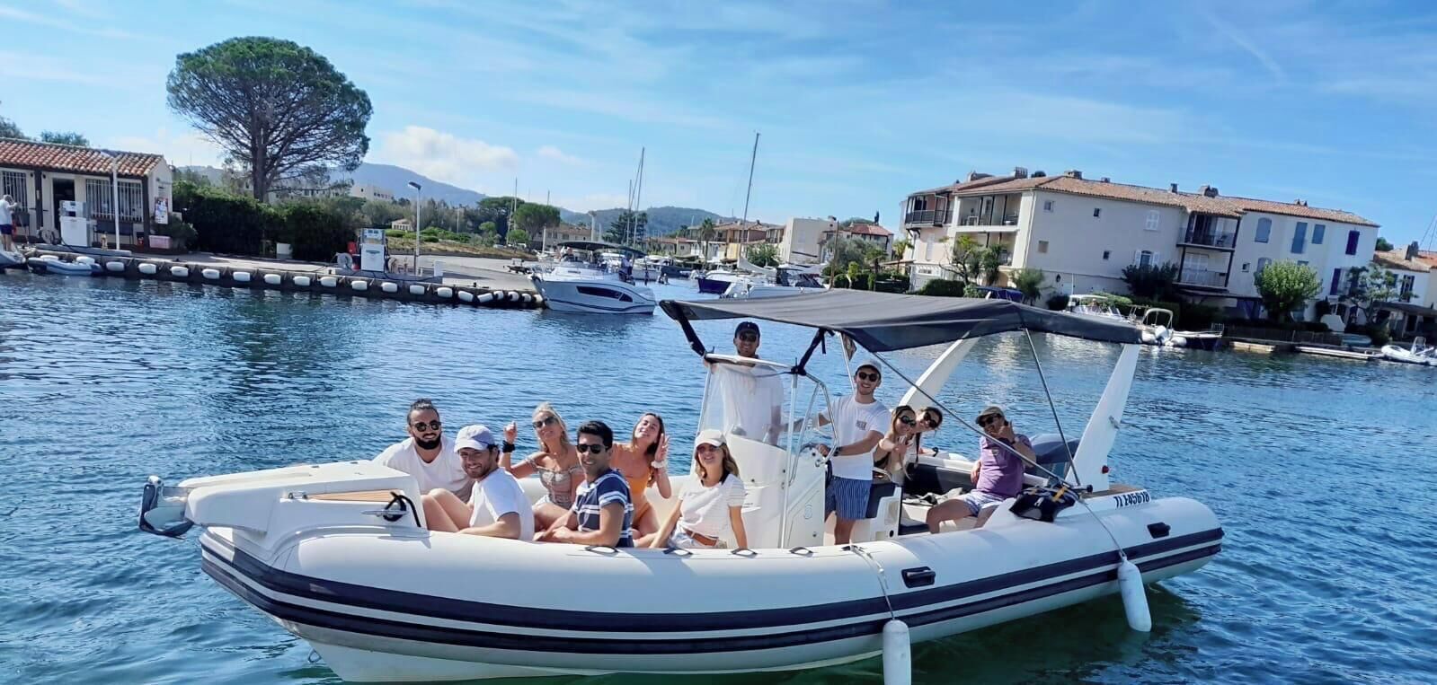 A group of people on a small motorboat with a canopy, docked at a marina with buildings in the background.