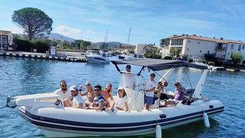 A group of people on a small motorboat with a canopy, docked at a marina with buildings in the background.