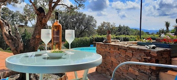 Una mesa con una botella y dos vasos, un muro de piedra, una estatua de Buda y una piscina al fondo.