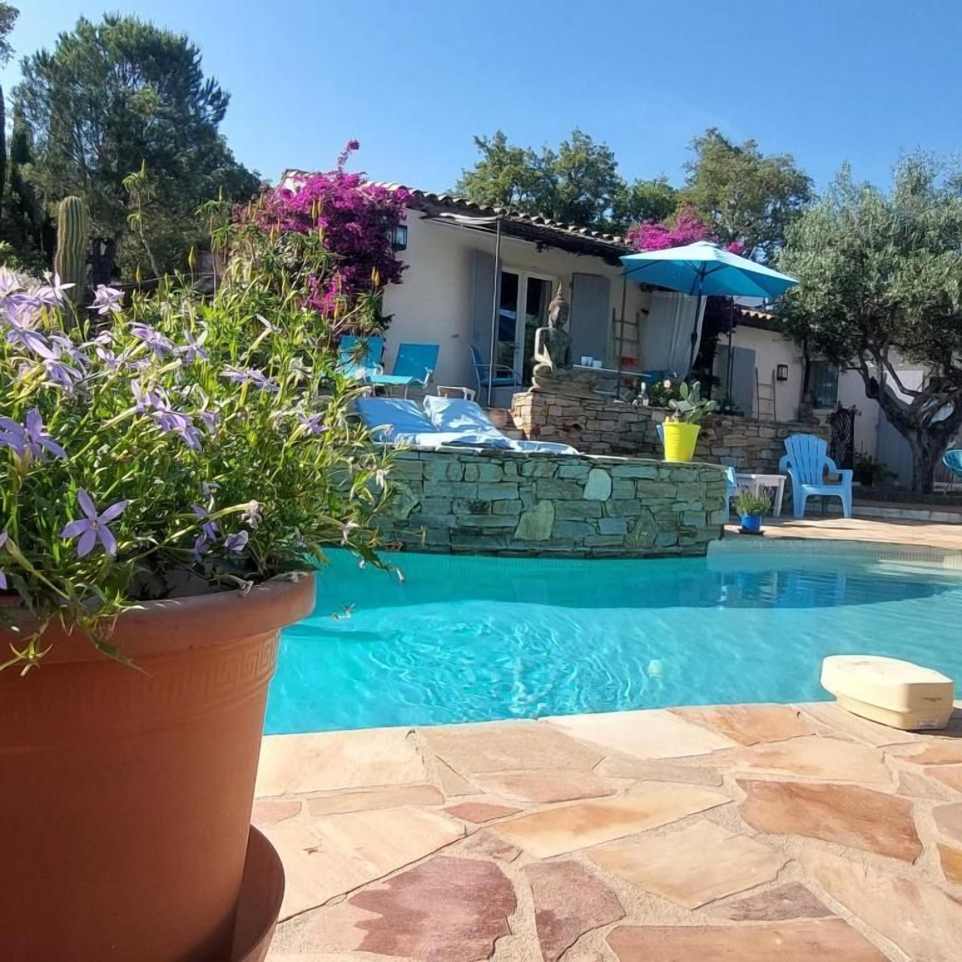 Piscina com azulejos de pedra, um vaso de planta e móveis de exterior.