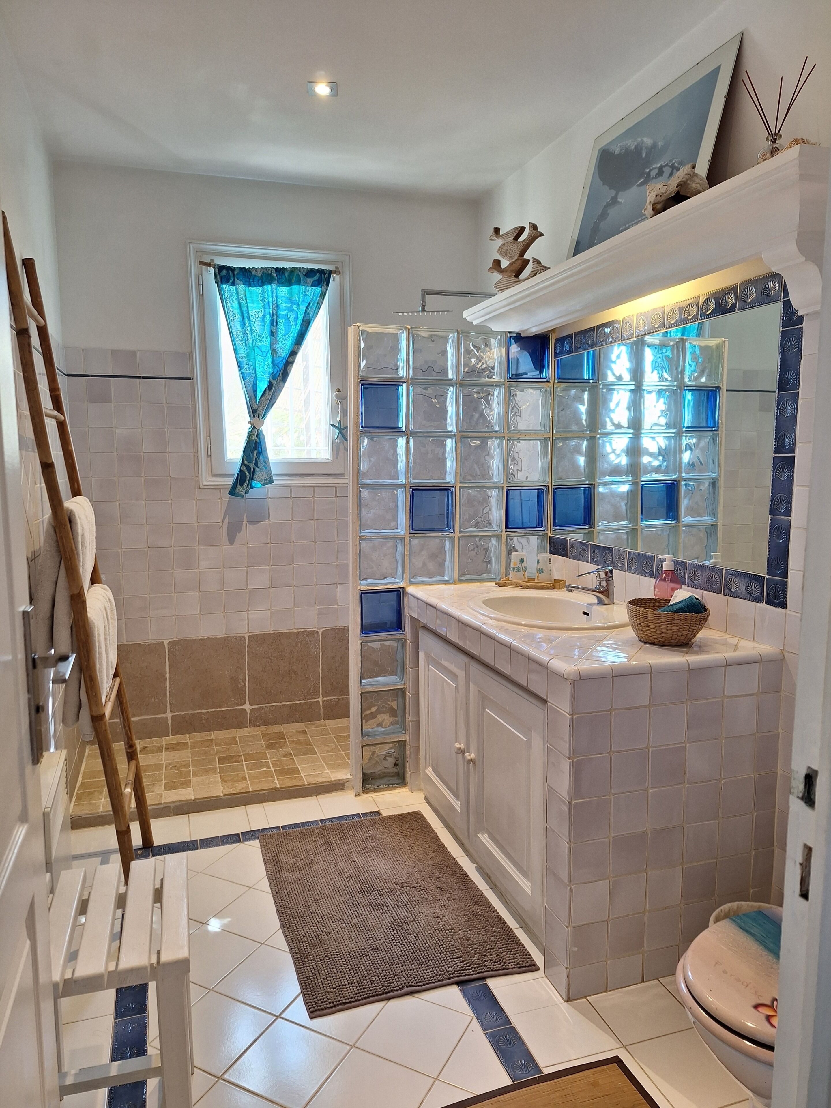 A bathroom with a shower, a sink, a mirror, and a window with curtains.