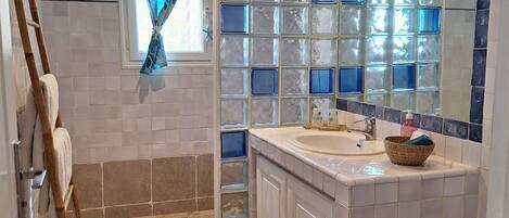A bathroom with a shower, a sink, a mirror, and a window with curtains.