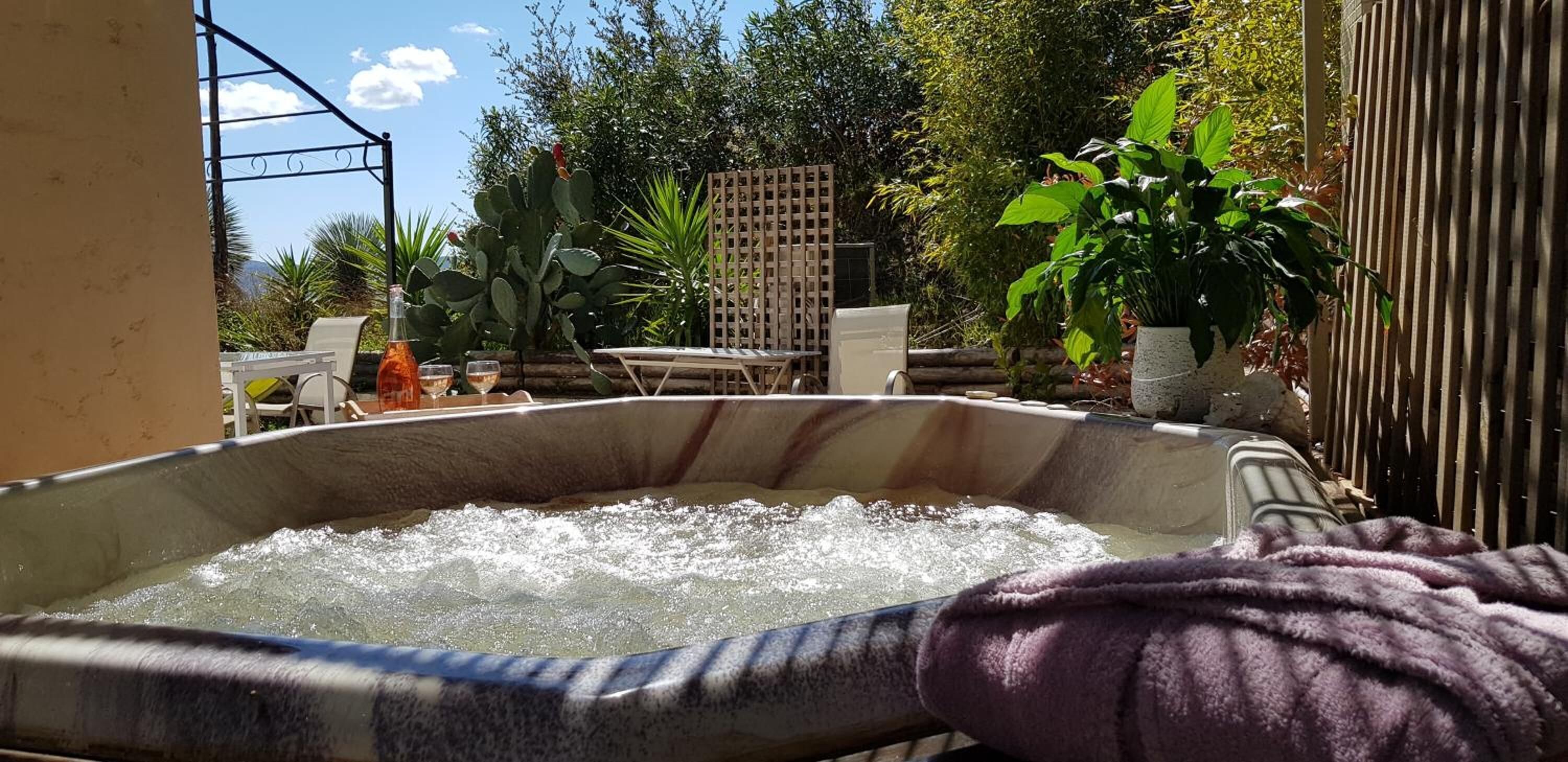 Ein Whirlpool in einer Außenanlage mit einer Terrassenfläche, umgeben von Pflanzen und einem Holzzaun.