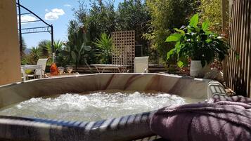 Ein Whirlpool in einer Außenanlage mit einer Terrassenfläche, umgeben von Pflanzen und einem Holzzaun.
