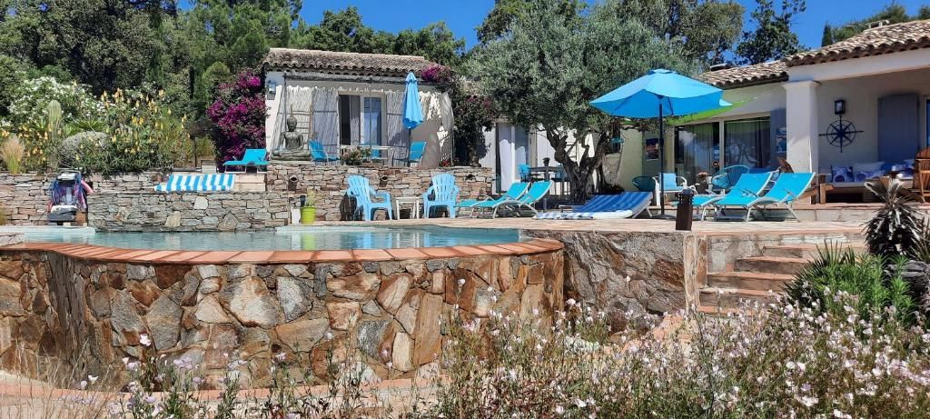 Zona de piscina con muros de piedra, sillas reclinables azules y un área de estar cubierta con sombrillas.