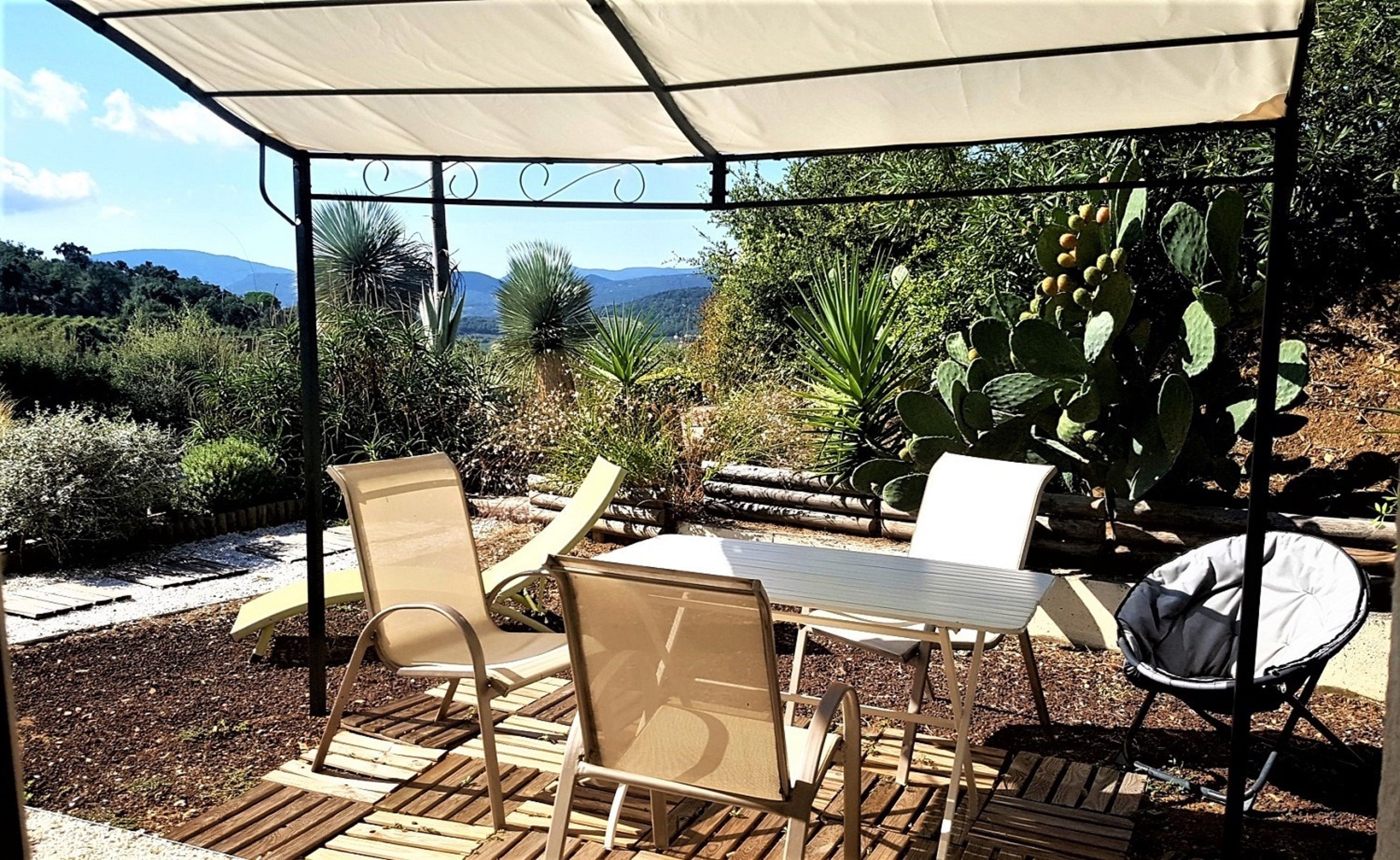 An outdoor patio with a table and chairs, a covered area, and a view of a mountainous landscape.