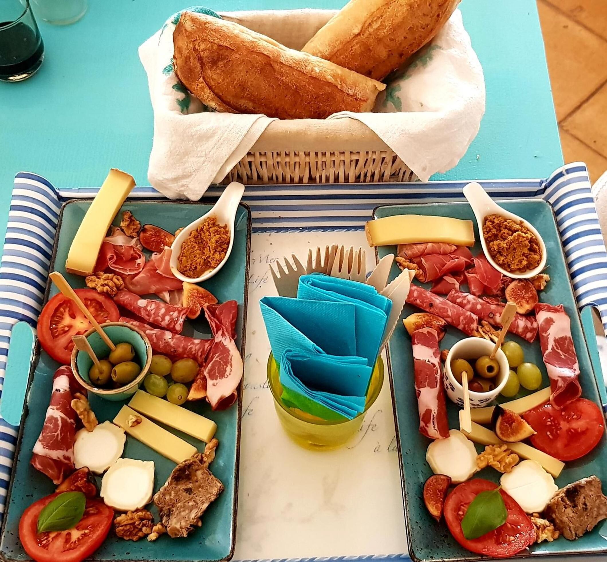 A charcuterie board with various meats, cheeses, and olives on a blue tablecloth.