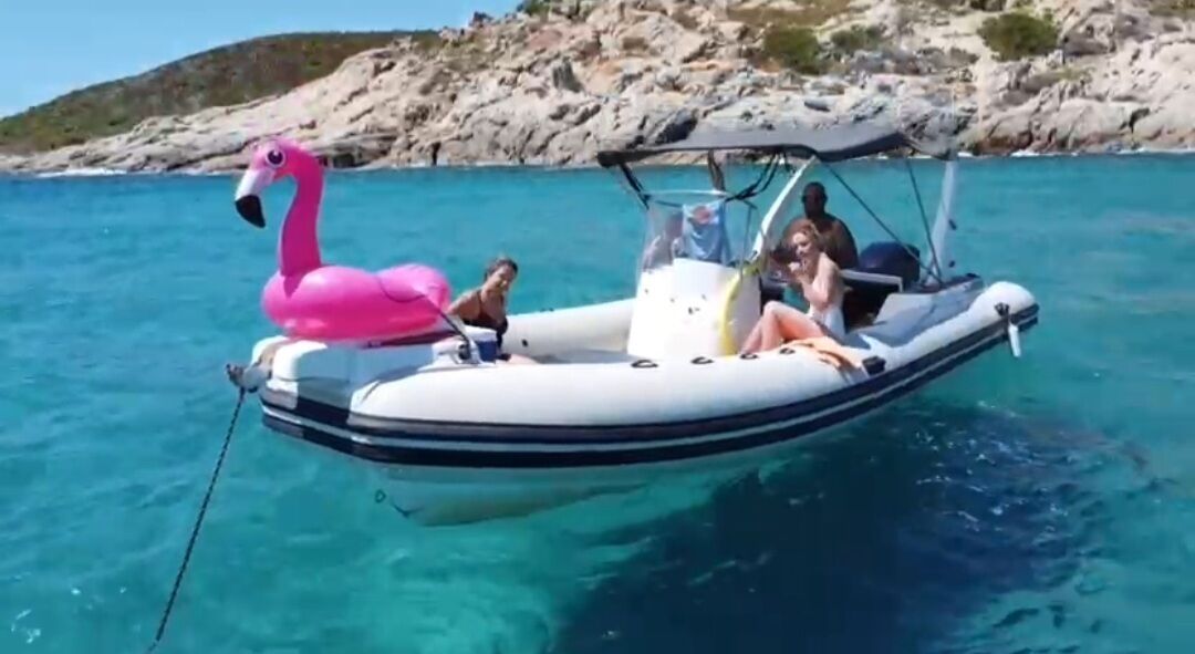 En båt dekorerad med en rosa flamingo, klart turkosfärgat vatten och ett bergigt landskap i bakgrunden.