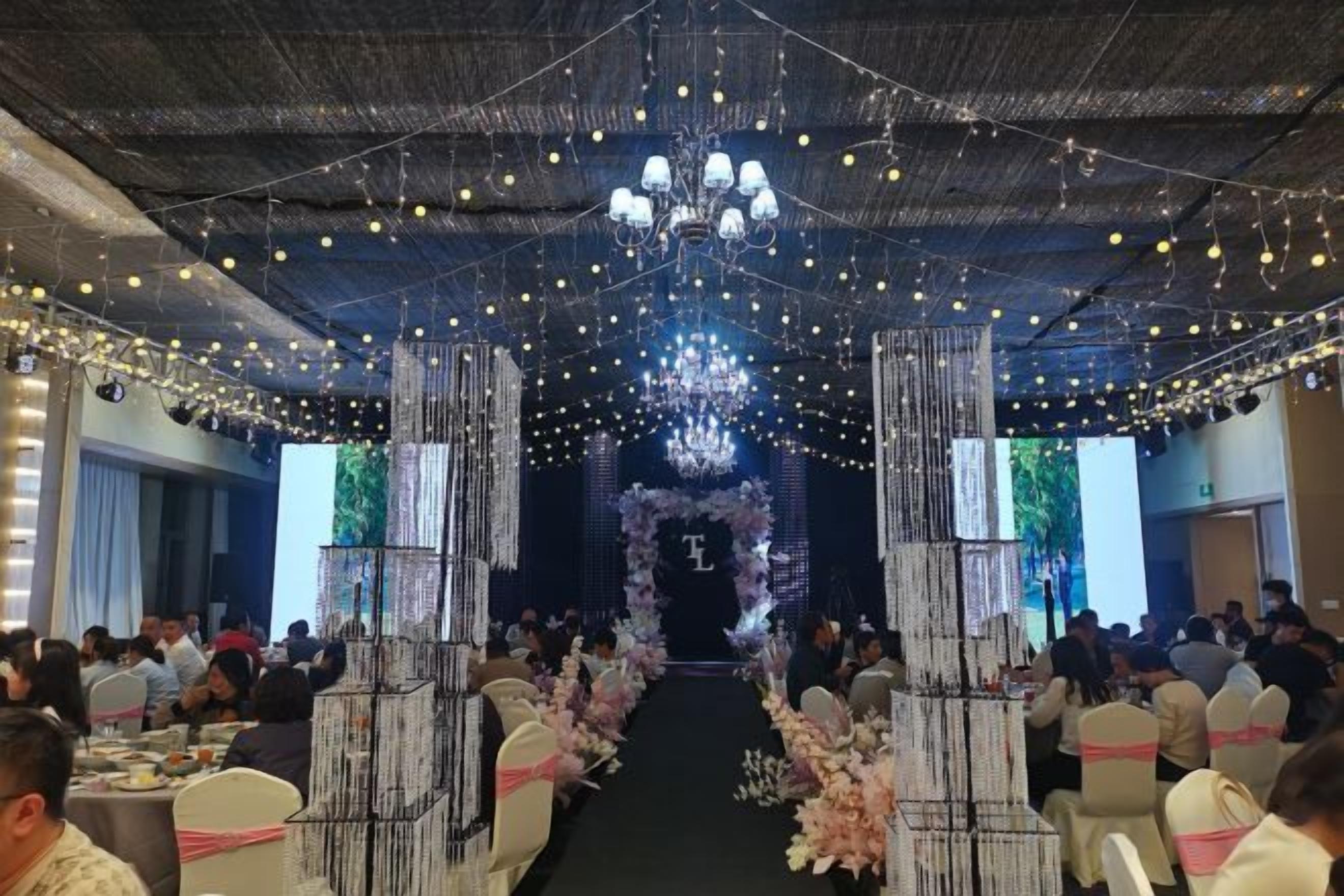 Un salón de banquetes con mesas dispuestas en filas, un pasillo central y una araña.