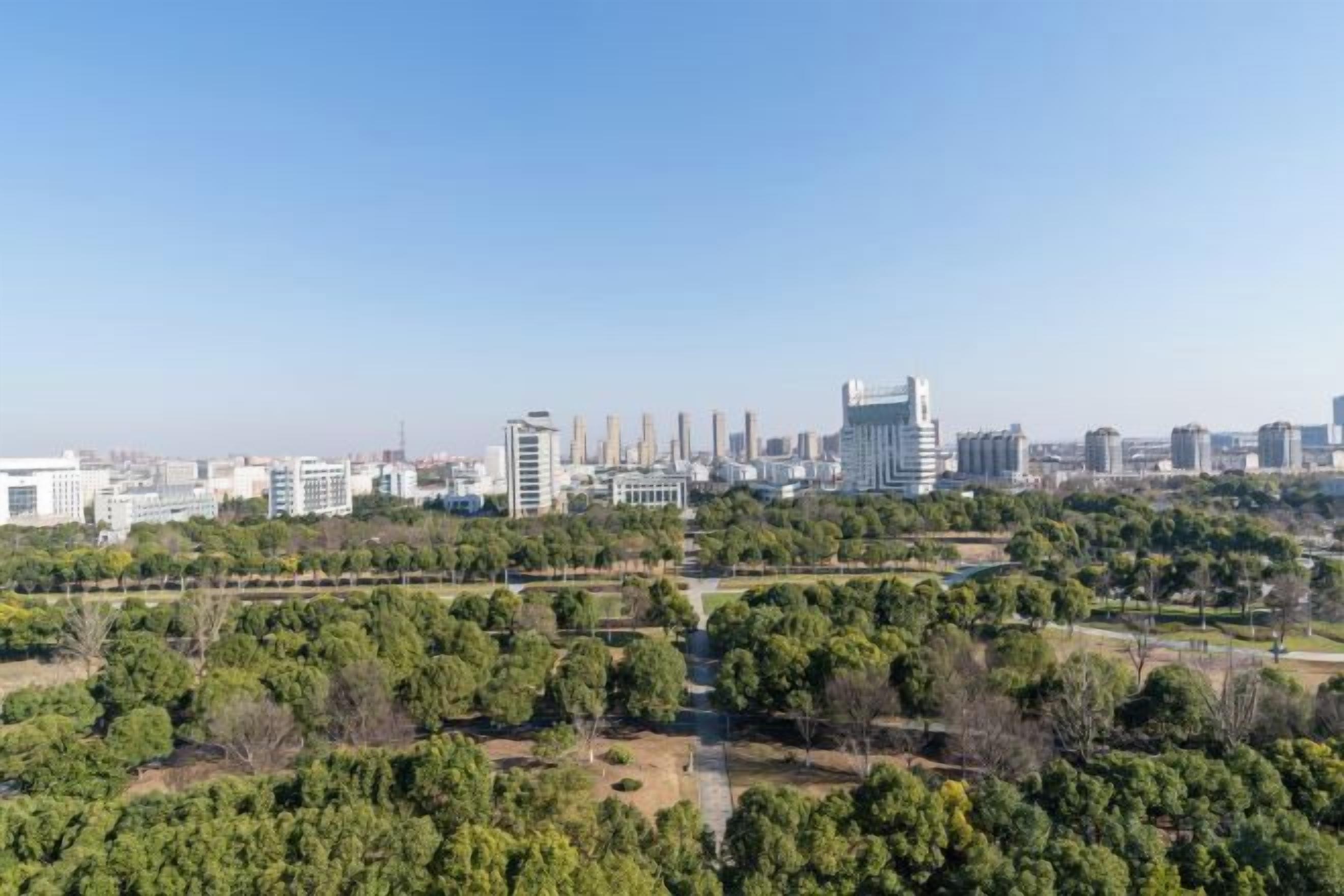 A cityscape with modern buildings, a park area with trees, and a clear sky.