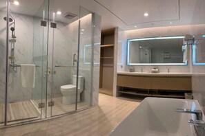 A modern bathroom with a glass-enclosed shower, a white toilet, a large mirror, and a freestanding bathtub.