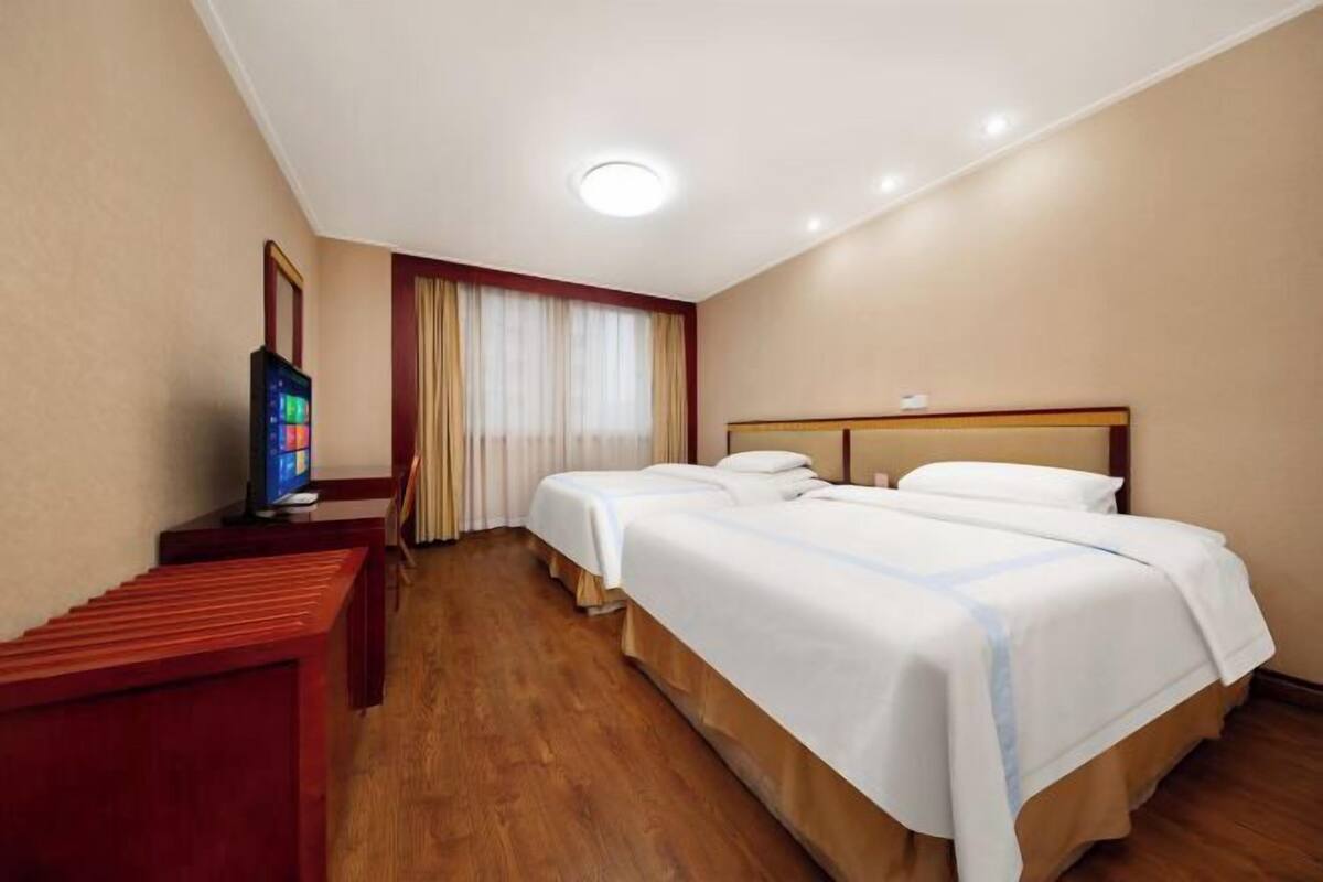 Una camera d'albergo con due letti, una televisione e una panca di legno.