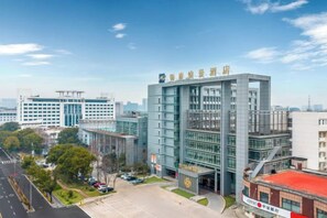 A modern building with a glass facade, surrounded by a parking lot and other buildings. - Jintai Metropark Hotel (Taizhou)