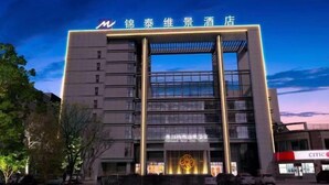 A modern hotel building with a prominent entrance and a large illuminated logo. - Jintai Metropark Hotel (Taizhou)