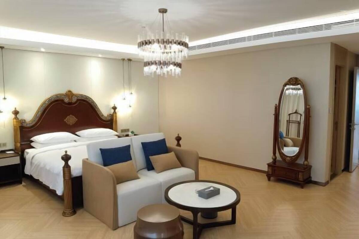 Una camera d'albergo con un letto, una poltrona, un tavolo rotondo, un lampadario e uno specchio.