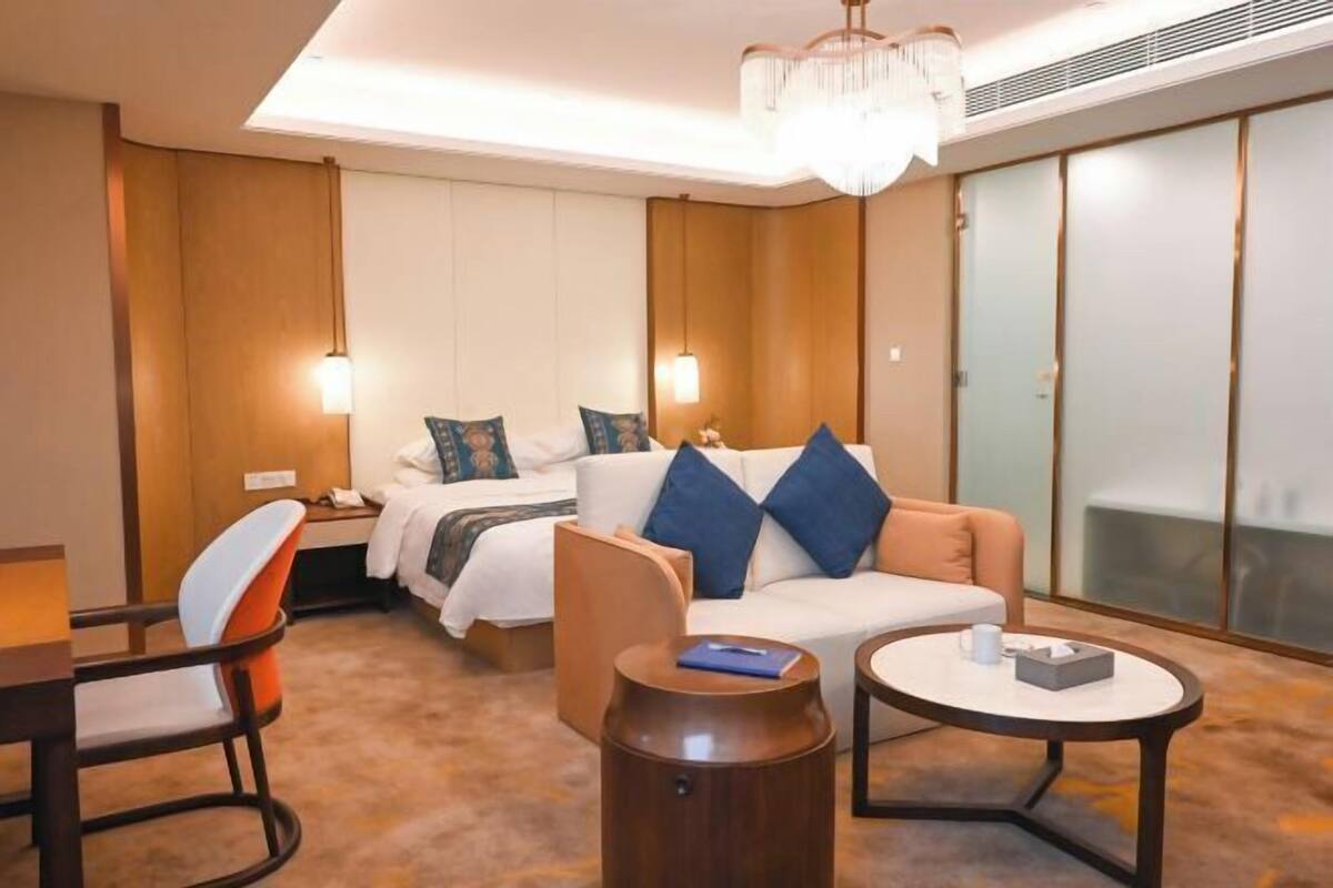 Una camera d'albergo con un letto, un divano, un tavolino rotondo, una sedia e un lampadario.